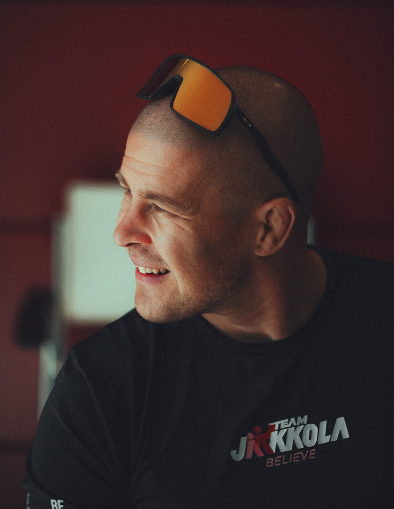 Valmentaja poseeraa itsevarmasti aurinkolasit päässään, katse suunnattuna kaukaisuuteen.